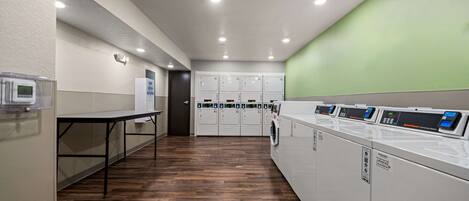 A laundry room with multiple washing machines, a drying rack, and a table with a control panel.