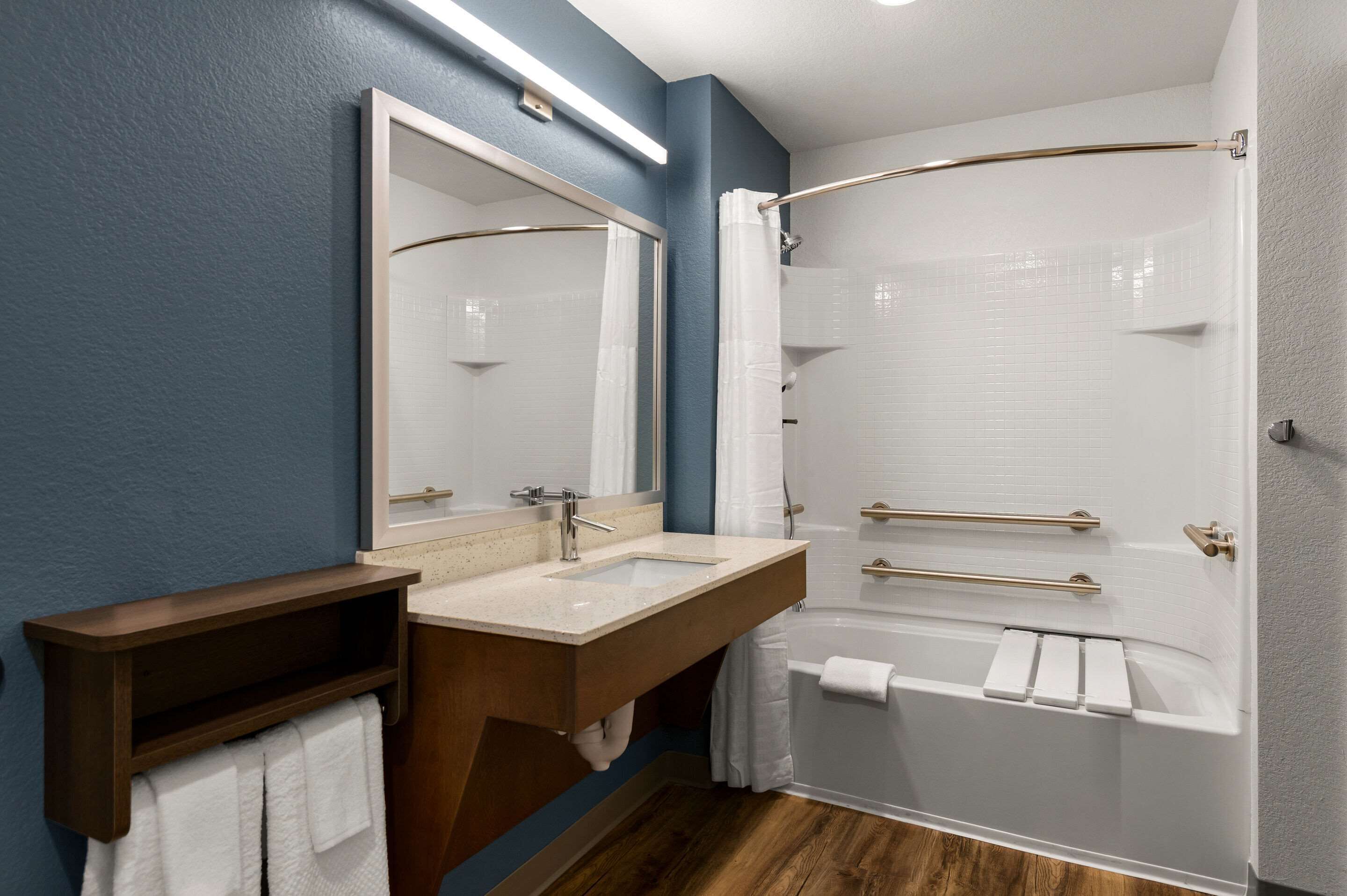 A modern bathroom with a wooden vanity, a large mirror, a bathtub, and a shower enclosure.