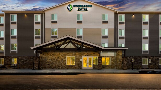 A multi-story hotel with a stone facade, a prominent sign reading "Woodspring Suites," and a covered entrance area.