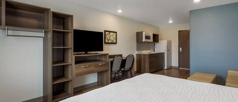 Een moderne hotelkamer met een groot bed, een bureau met een flatscreen televisie, een kitchenette en een zithoek met stoelen.