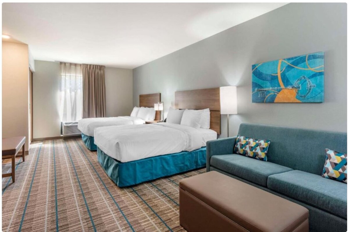 Une chambre d’hôtel avec deux lits, un canapé, un banc et un tableau au mur.