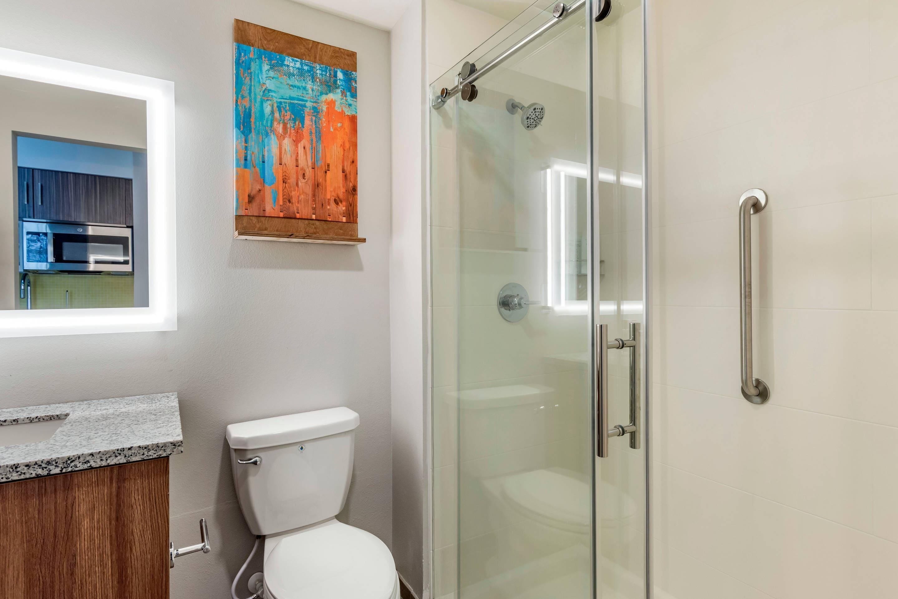 Een moderne badkamer met een douchecabine van glas, een wit toilet en een granieten aanrechtblad.
