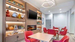 Een moderne eetruimte met rode stoelen en een houten tafel, omringd door planken met decoratieve objecten en een flatscreen televisie.