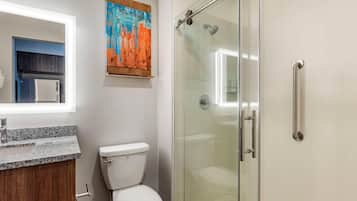 Un baño con cabina de ducha de vidrio, inodoro blanco, lavabo con encimera de granito y mueble de madera.