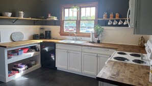 A modern kitchen with a dishwasher, stove, and a window overlooking a parking lot. - Ranch House at Edelweiss Winery & Events (Hermann)