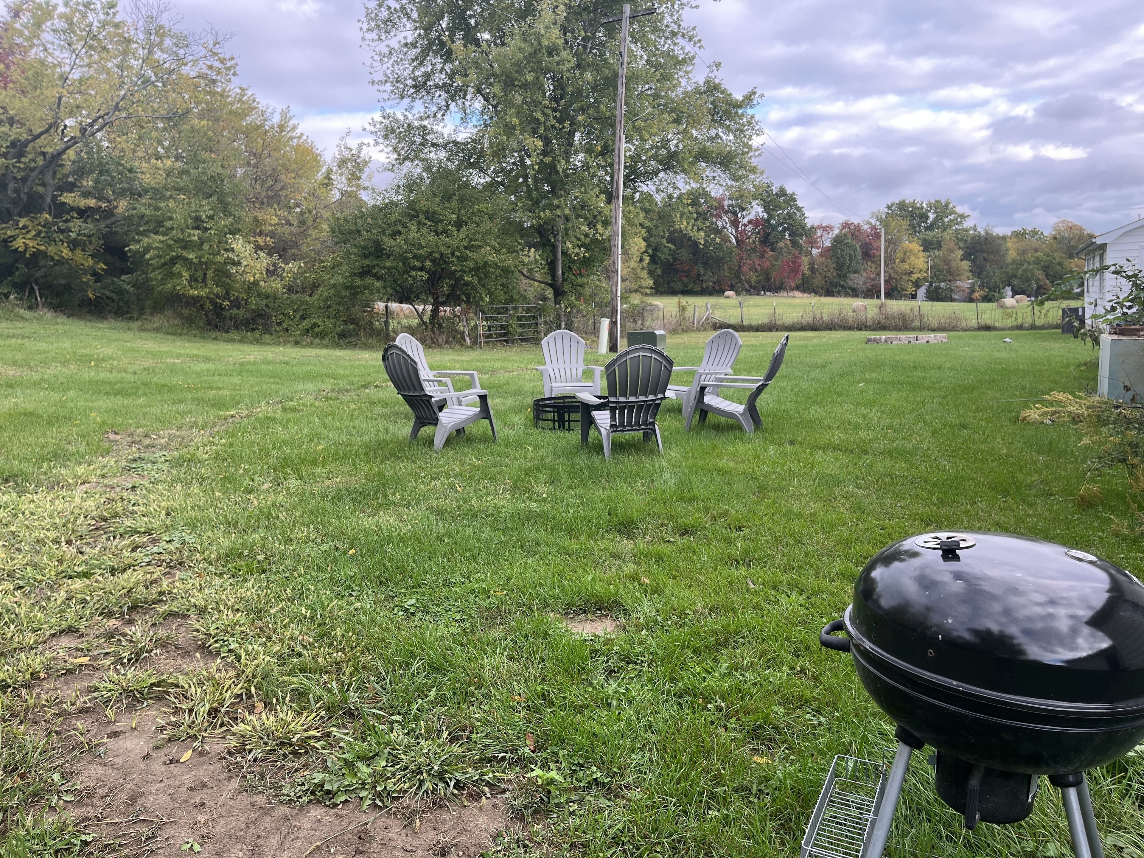 A grassy backyard with a barbecue grill, a table, and four Adirondack chairs.