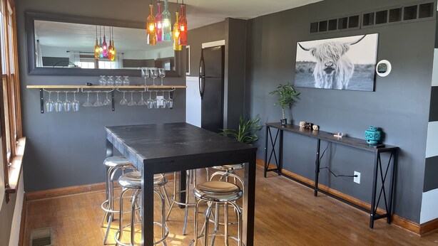 A modern kitchen with a dark countertop, bar stools, and a hanging wine rack. - Ranch House at Edelweiss Winery & Events (Hermann)