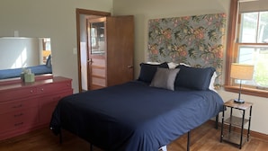 A bedroom with a bed, a dresser, a ceiling fan, a window with a view, and a wall with a floral pattern. - Ranch House at Edelweiss Winery & Events (Hermann)