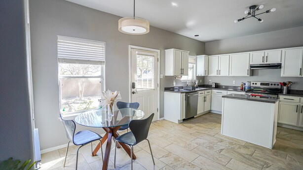 A modern kitchen with white cabinets, a dining table with chairs, and a large window with blinds. - Ideally Located, Stone Oak Extended Family Stay (San Antonio)