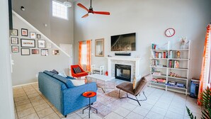 A living room with a blue sofa, a red chair, a fireplace, a bookshelf, and a TV mounted on the wall. - Ideally Located, Stone Oak Extended Family Stay (San Antonio)