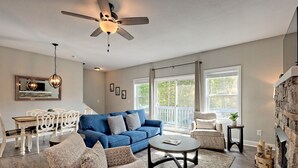 Un salon avec un canapé bleu, des fauteuils à motifs, une table basse, un ventilateur de plafond et une cheminée.