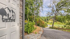 Une porte de garage ornée d’une pancarte de bienvenue, avec vue sur un terrain de golf et des arbres.