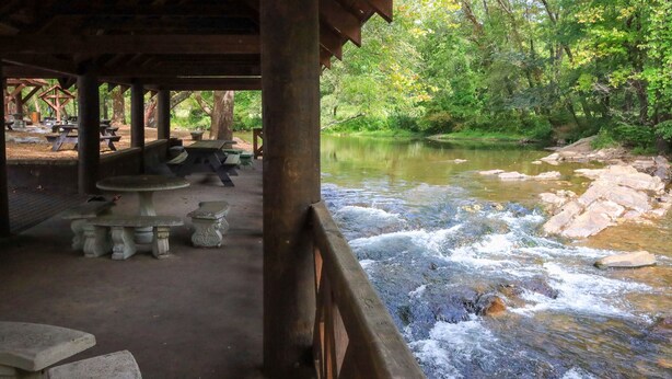 Un pavillon au bord de la rivière, équipé de tables de pique-nique et offrant une vue sur le cours d’eau.