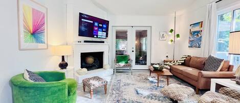 A living room with a fireplace, a television mounted on the wall, a green armchair, a brown sofa, and a patterned rug.