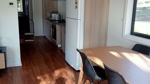 A modern kitchen with wooden cabinets, a white refrigerator, and a dining area with a table and chairs. - Wedderburn Caravan Park (Wedderburn)