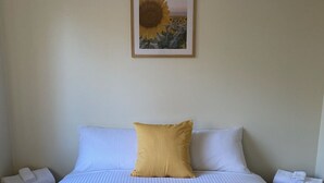 A neatly made bed with a striped white duvet, a mustard-colored pillow, and a large sunflower painting above it. - Wedderburn Caravan Park (Wedderburn)