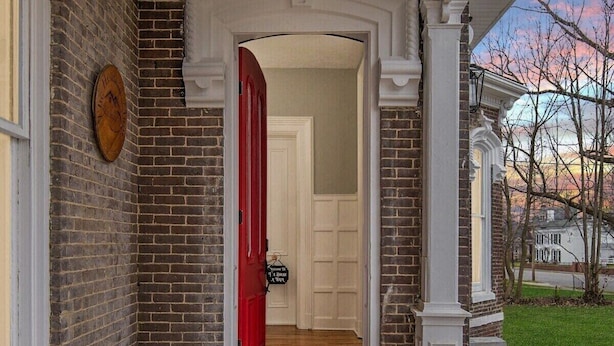 A wooden deck leading to a red door, brick walls, and a white door in the background.