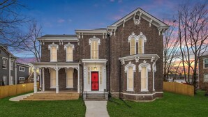 A two-story brick house with a front porch, a red door, and a well-maintained lawn.
