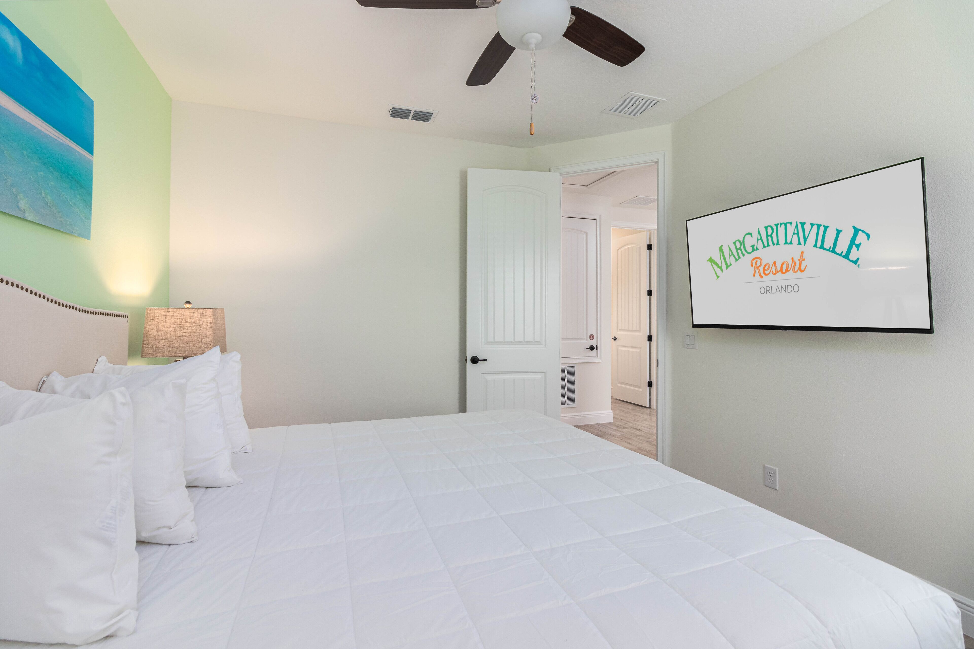 A hotel room with a bed, a ceiling fan, a painting, and a sign for Margaritaville Resort.
