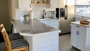 A kitchen with white cabinetry, a granite countertop, a built-in sink, a coffee maker, and a refrigerator.