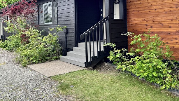 A two-story house with a dark exterior, a wooden side panel, and a front porch with a staircase.