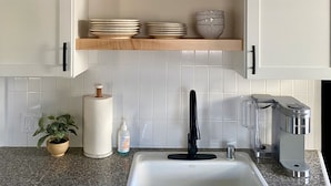 A kitchen with white cabinets, a granite countertop, a sink, a coffee maker, and decorative items on shelves.