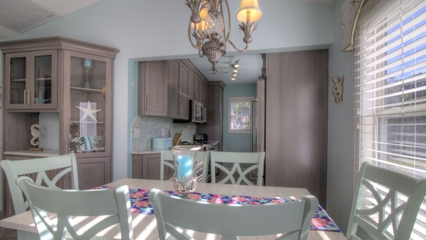 A dining area with a table set for four, surrounded by white chairs, and a chandelier above.