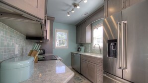 A modern kitchen with stainless steel appliances, a light blue tiled backsplash, and a window providing natural light.