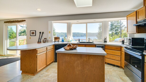 A modern kitchen with a large island, wooden cabinets, a built-in oven, and large windows offering a view of the outdoors. - Hoodsport Vacation Rental w/ Deck & Canal Views! (Hoodsport)