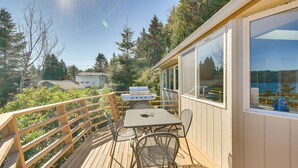 A wooden deck with a table and chairs, a grill, and a view of trees and a house in the background. - Hoodsport Vacation Rental w/ Deck & Canal Views! (Hoodsport)