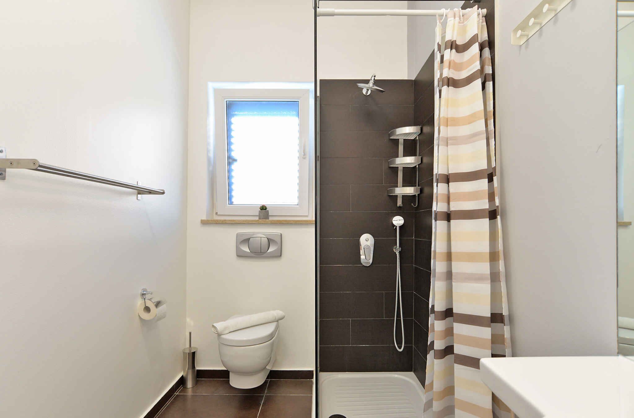 Un bagno con il water, una doccia con tenda a righe, una finestra e un portasciugamani.
