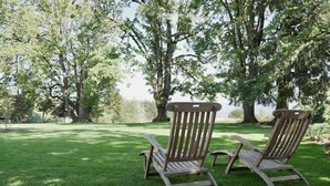 Deux fauteuils à bascule en bois sont placés sur une pelouse verdoyante, avec des arbres en arrière-plan.