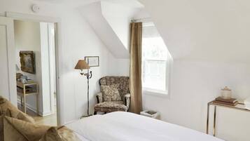 A bedroom with a bed, a chair, a lamp, a side table, and a window.