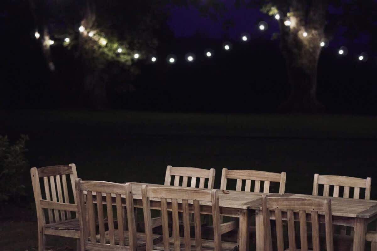 Ein Holzespeisetisch mit sechs Stühlen, umgeben von Lichterketten, draußen bei Nacht.