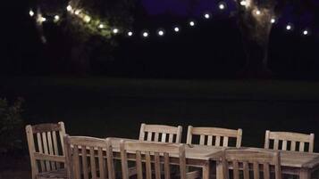 Ein Holzespeisetisch mit sechs Stühlen, umgeben von Lichterketten, draußen bei Nacht.