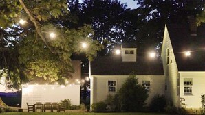 Un bâtiment blanc doté d’un toit à forte pente et d’une structure imposante qui ressemble à une tour. On peut voir des lampadaires et un espace avec des bancs à l’extérieur.