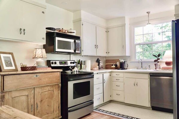 Een moderne keuken met witte kasten, een zwarte kookplaat en een magnetron. Er is een raam dat natuurlijk licht en uitzicht op groen biedt.