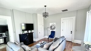 Una sala moderna con un sofá modular, una mesa de centro de cristal, una chimenea, un televisor y un comedor con una mesa redonda.
