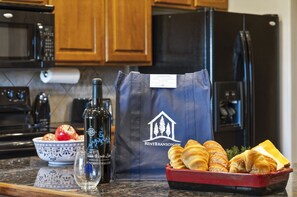 A kitchen counter with a bottle of wine, a bowl of fruit, a bag with a logo, and a tray of pastries. - Gated Community_Onsite Golf Course_Hot Tub_Air Hockey_Foosball_Board Games_Free SDC Tickets (Reeds Spring)