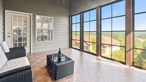 A covered patio with wicker furniture, a ceiling fan, and large windows offering a view of the surrounding landscape. - Gated Community_Onsite Golf Course_Hot Tub_Air Hockey_Foosball_Board Games_Free SDC Tickets (Reeds Spring)