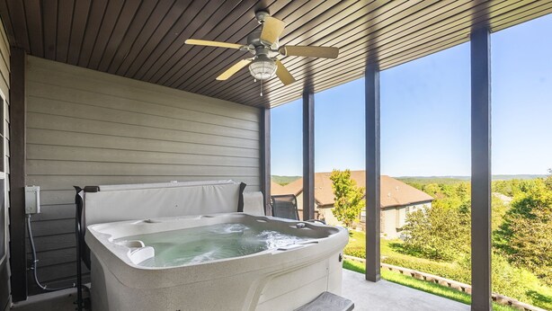 Un jacuzzi bajo una pérgola de madera con ventilador de techo, con vistas a una zona residencial.