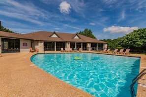 A swimming pool with lounge chairs and a building with a stone facade and a pitched roof. - Gated Community_Onsite Golf Course_Hot Tub_Air Hockey_Foosball_Board Games_Free SDC Tickets (Reeds Spring)