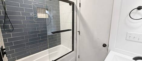 A bathroom with a glass-enclosed shower, white tiled walls, a white sink, and a marble floor.