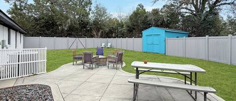 A backyard with a picnic table, chairs, and a shed.