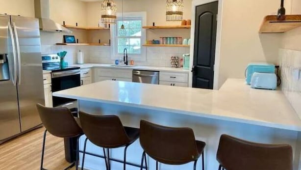 A modern kitchen with a large island, bar stools, stainless steel appliances, and pendant lighting.