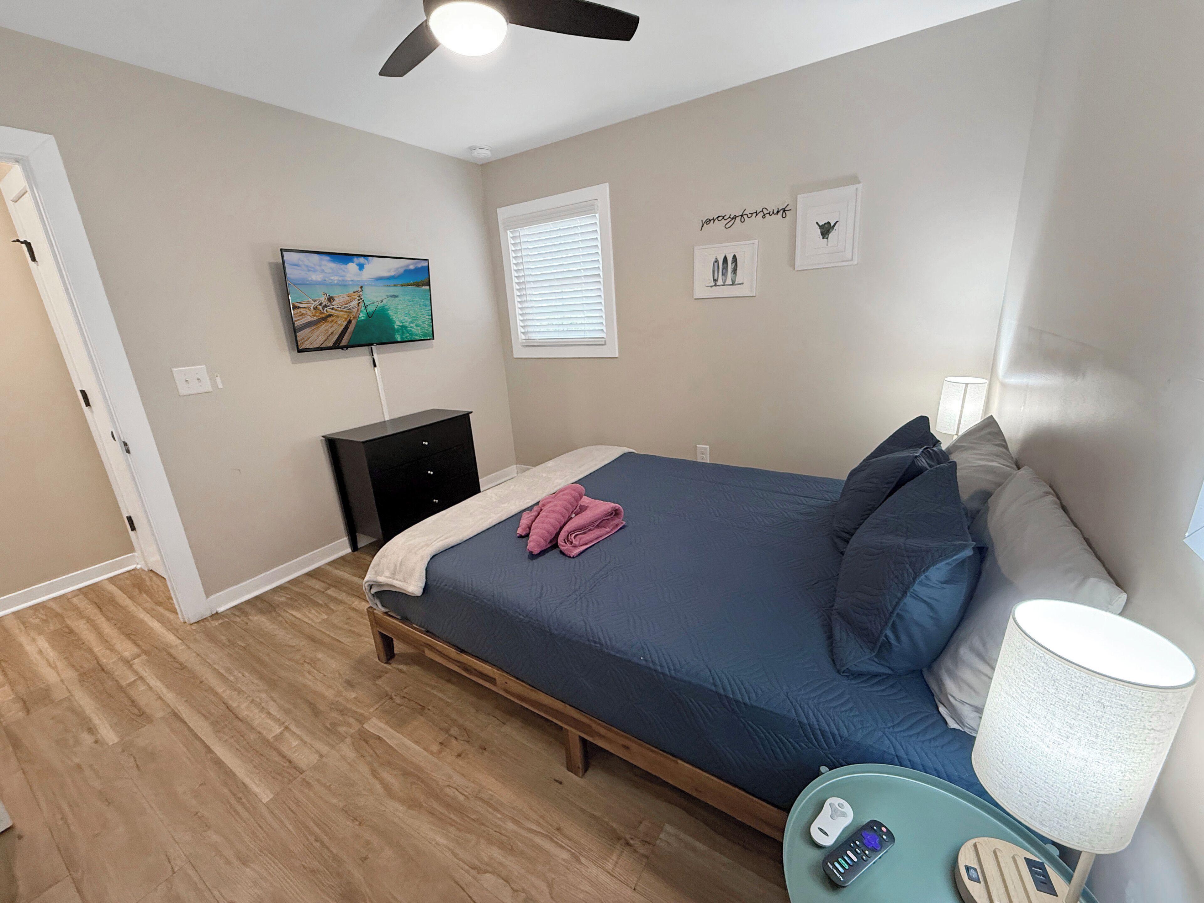 A bedroom with a bed, a TV, a bedside table with a lamp, and a window with blinds.