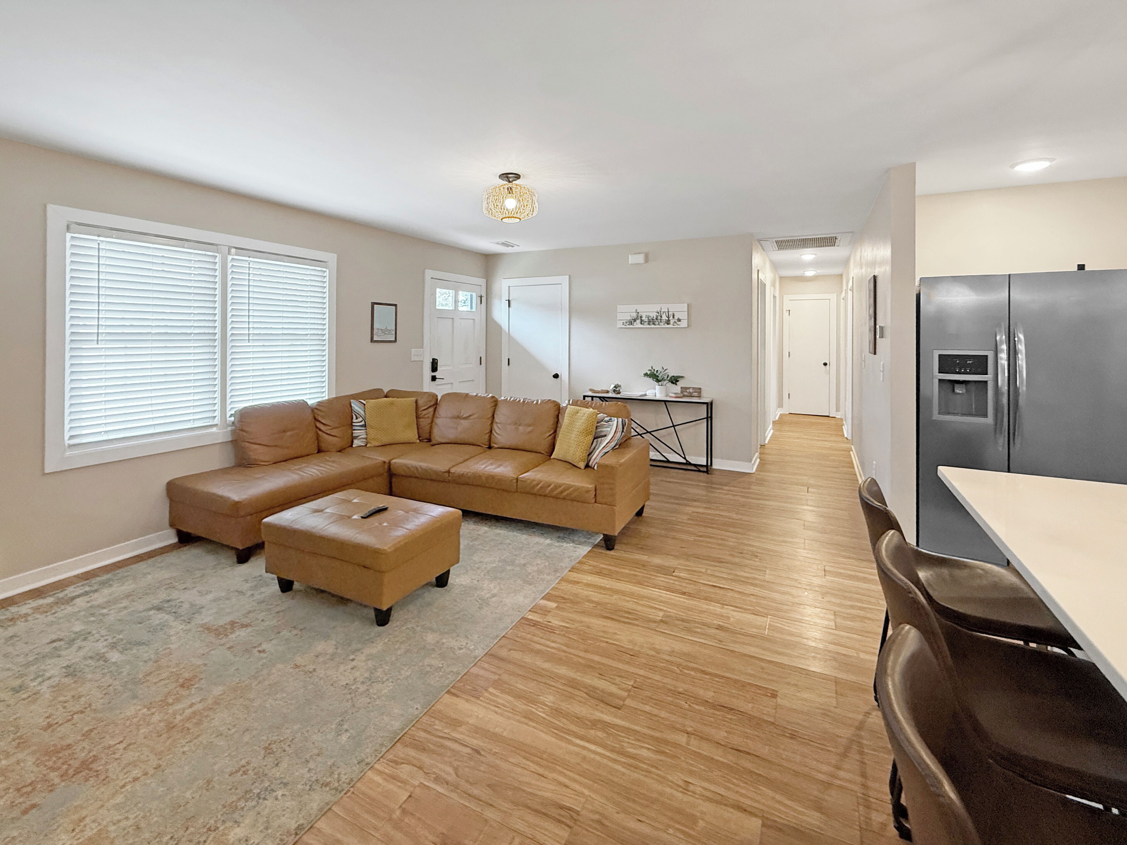 A spacious living room with a large L-shaped sectional sofa, a small ottoman, and a dining area with a table and chairs.