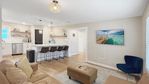 A modern living room with a beige sofa set, a blue armchair, and a dining area with bar stools.