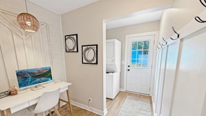 A modern room with a white desk, a computer, a wall-mounted TV, and a door leading to a balcony.