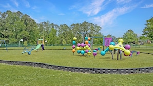A playground with various play structures, a basketball hoop, and a fenced area.
